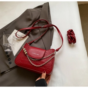 Detailed view of red crocodile textured shoulder bag with silver chain and bead accents