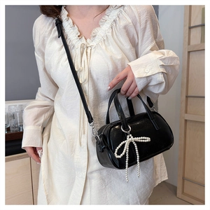Detail of glossy black crossbody bag with pearl bow charm worn by a model