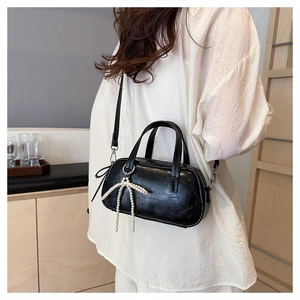 Close-up of black glossy mini barrel bag featuring a pearl bow pendant and silver hardware
