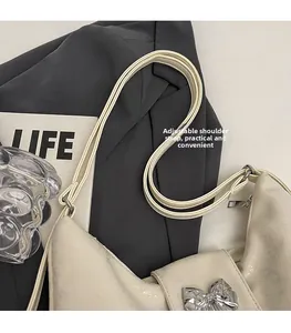 Close-up of cream faux leather tote featuring a silver metal bow and adjustable strap