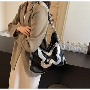 Close-up of black glossy tote bag featuring a silver butterfly patch and metal studs