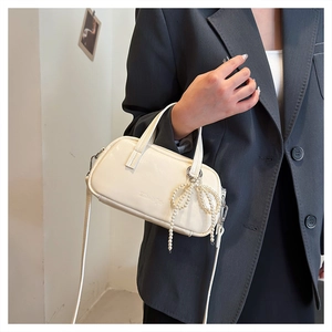 Detail of cream mini bowling bag with pearl bow charm and crossbody strap on suit jacket