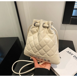 Detail of cream quilted bucket backpack featuring silver metal logo and heart pendant charm