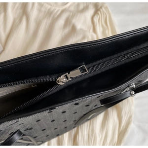 Close-up of black tote bag zipper with floral fabric texture and leather trim details