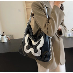 Detailed view of shiny black tote bag with large silver butterfly and metal chain