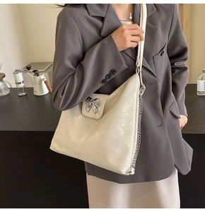 Detail of a creamy white pearlescent tote bag with a silver bow lock and chain strap