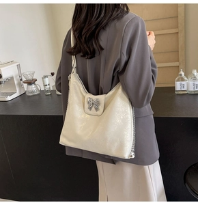 Detail of a pearlescent tote bag featuring a metallic silver bow and chain strap