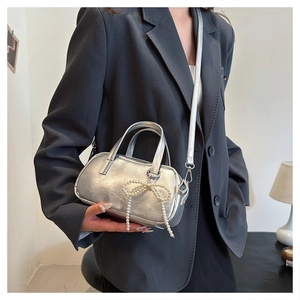 Detail of silver metallic handbag with pearl bow pendant worn with a grey suit blazer