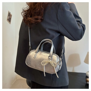 Detail of silver metallic crossbody bag featuring wrinkled texture and pearl bow charm