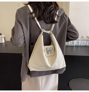 Close-up of cream white tote bag with glossy pleated texture and silver bow detail