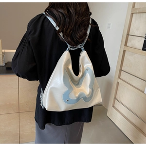 Detail showing high-capacity cream tote bag with blue butterfly patch and silver rivets