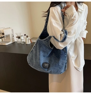 Détail du sac cabas en jean bleu avec patch nœud en cuir montrant le grand volume de côté