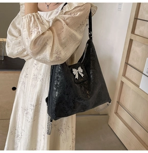 Close-up of black glossy tote bag with silver bow detail and chain on shoulder