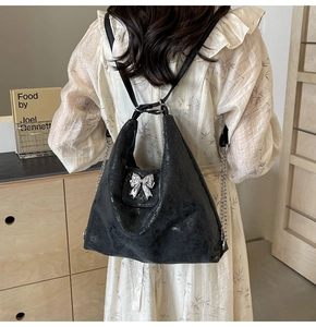 Detail of black textured leather tote with silver bow and chain strap on a model