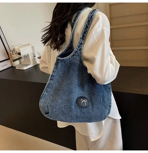 Vue détaillée du grand sac cabas en denim bleu avec écusson nœud blanc porté par le mannequin