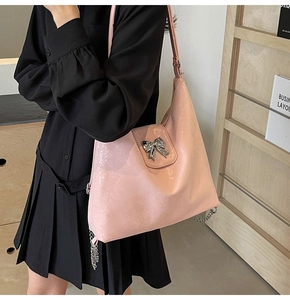 Detail of pink hobo bag with metallic bow and chain, shown worn by a model