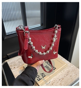 Detail of red bucket bag featuring silver butterfly charms and beaded chain handle
