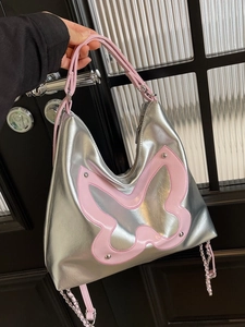 Silver metallic tote bag with pink butterfly detail and studs, shown in hand for commute