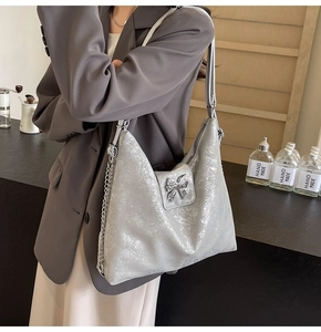 Detail view of silver tote bag featuring a metallic bow and chain strap on a desk
