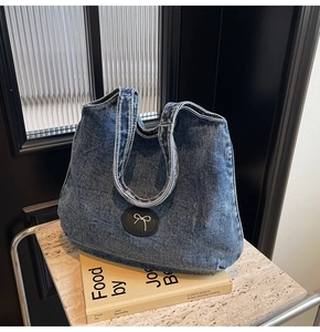 Détail du sac cabas en denim bleu avec écusson papillon sur une surface en pierre