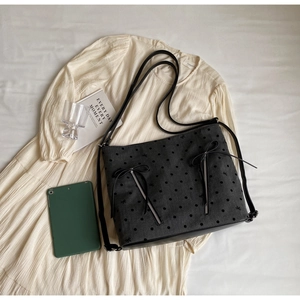 Detail of grey polka dot tote bag with bow decoration and zippers over a beige dress