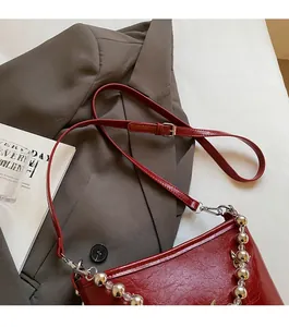 Detail of red leather shoulder bag with decorative ball chain and adjustable strap