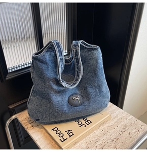 Détail du sac cabas en denim bleu avec nœud en métal argenté et patch en cuir