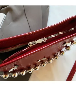 Close-up of a red patent leather bucket bag featuring a smooth silver zipper and metallic beads