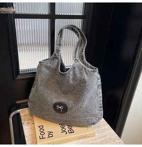 Détail du cabas en denim gris rétro avec patch en cuir noir et nœud métallique sur marbre