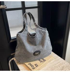 Détail du sac cabas en denim gris délavé avec écusson en cuir et nœud argenté décoratif