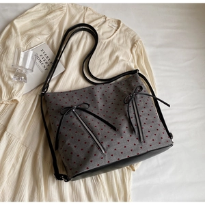 Detail of grey tote bag with red heart print, black bows, and faux leather base