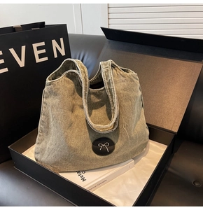 Détail d'un sac cabas en denim délavé avec patch nœud argenté et bords effilochés