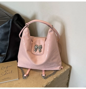 Detail of pink glossy tote backpack with silver bow decoration on stone surface