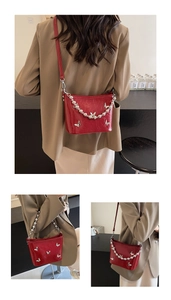 Close-up of red patent leather shoulder bag with silver butterfly charms and pearl chain