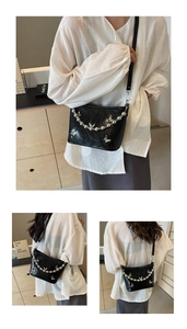 Detail of black crossbody bucket bag with silver butterflies and pearl chain strap