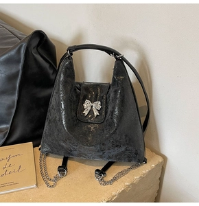Detail of black textured leather bag with silver bow ornament on a stone platform