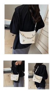 Close-up of white glossy shoulder bag featuring silver butterfly charm and metal bead chain