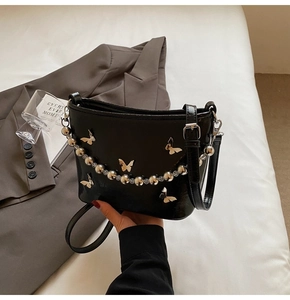 Detail of black glossy leather bucket bag with silver butterfly charms and bead chain