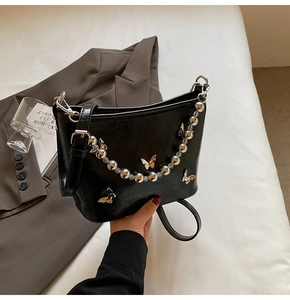 Detail of black glossy bucket bag featuring silver butterfly charms and decorative bead chain
