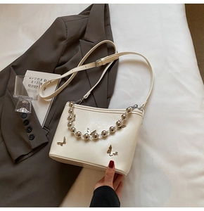 Detail of cream white bucket bag featuring silver butterfly charms and beaded chain strap