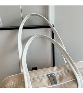 Detail of beige tote bag featuring smooth white shoulder straps and silver metal zippers