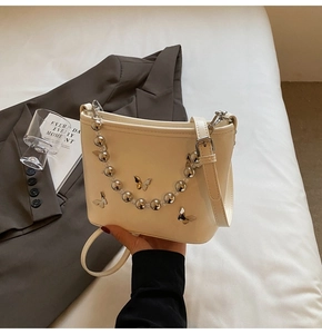 Detail of white bucket bag featuring a 3D metal butterfly and beaded handle chain