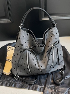 Chic grey tote bag with black polka dots and leather bows on a dark leather background