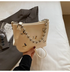 Detail of cream leather handbag featuring silver bead chain and metal butterfly accents
