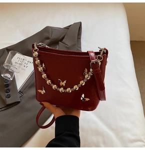 Detail of burgundy shoulder bag with silver metal butterfly and beaded chain strap