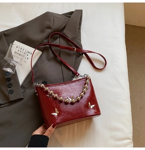 Close-up of dark red bucket bag with silver butterfly hardware on grey suit fabric