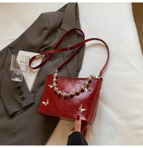 Detail of burgundy patent leather bucket bag with silver butterfly and bead handle