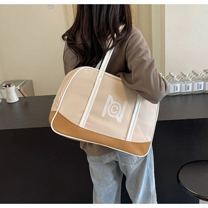 Large beige canvas tote bag with brown leather corners shown in a lifestyle shoulder view