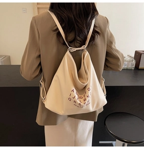 Detailed view of beige convertible tote bag with stylish dark curved letter prints