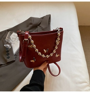 Detail of burgundy leather bucket bag with silver butterfly chain and floral accents
